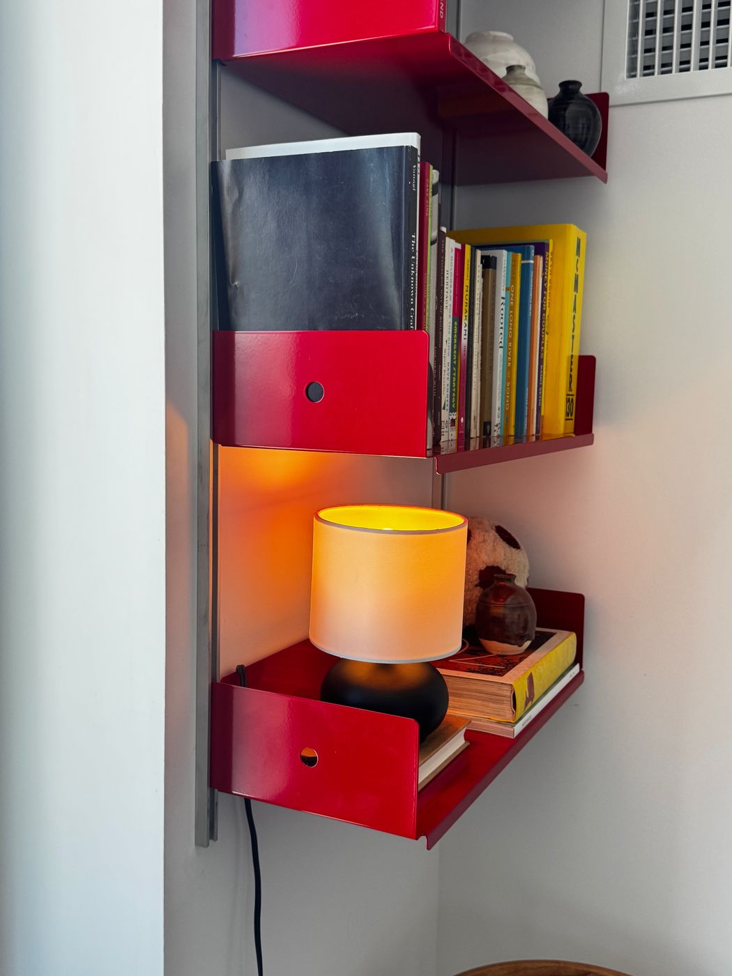 Red shelves mounted in a corner with a lamp and books